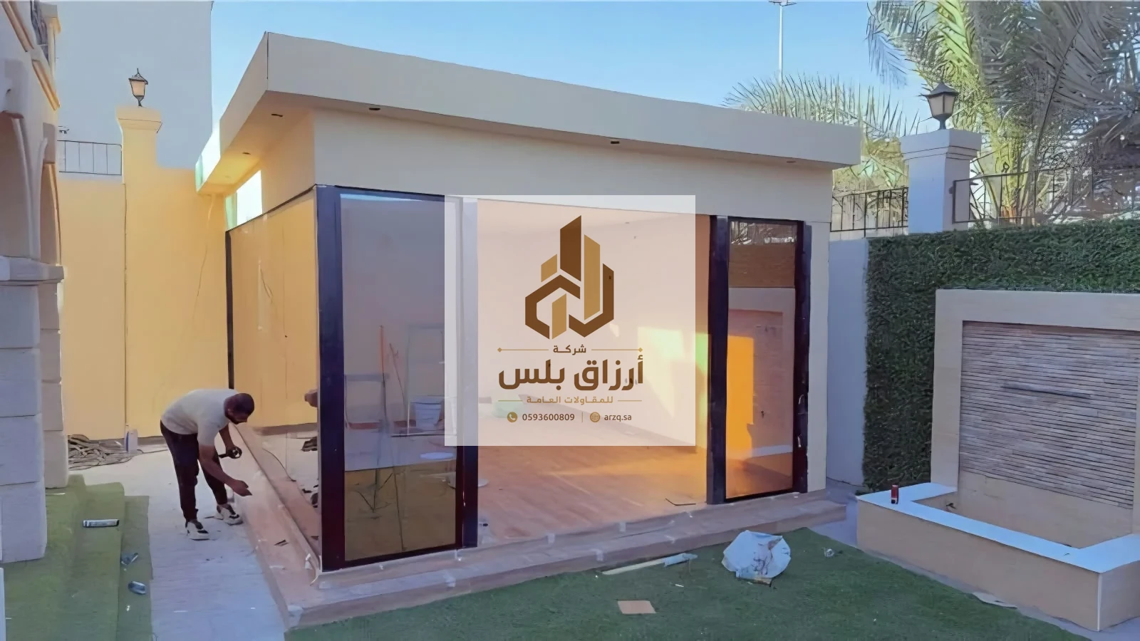 ملحق من ألواح ساندوتش بانل بجدران خارجية فاتحة وواجهات زجاجية بإطارات ألمنيوم داكنة في حديقة فيلا