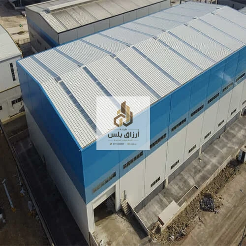 منظر جوي لمبنى صناعي بواجهة ألواح باللونين الأزرق والأبيض وسقف من ألواح معزولة مضلّعة