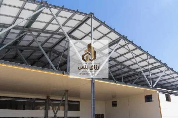 الوجه السفلي لسقف من ألواح معزولة مثبّت على جمالونات معدنية أعلى جدران من الألواح في منشأ مفتوح