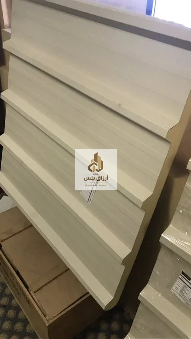 ألواح ساندوتش بانل بلون كريمي مكدّسة بشكل مائل تُظهر حافة التعشيق وبطاقة بيانات ملصقة على أحد الألواح