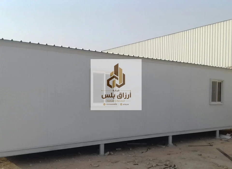 وحدة طويلة من ألواح الساندوتش بانل بوجه أبيض مرفوعة على قواعد معدنية وبها نافذة وباب في موقع عمل