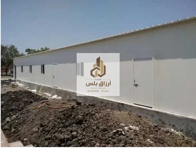 مبنى طويل مكسو بألواح معزولة يستقر على قاعدة خرسانية مرتفعة وبه أبواب ونوافذ مع تربة محفورة أمامه