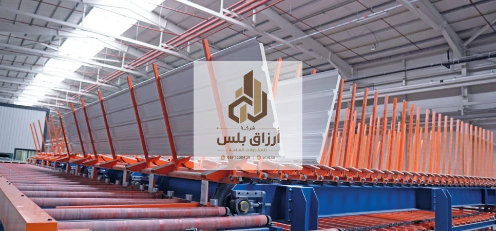 خط إنتاج ألواح داخل مصنع بناقل طويل وأذرع مناولة برتقالية ترفع لوحًا جاهزًا