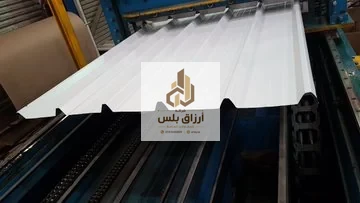 لوح ساندوتش بانل أبيض مضلّع يخرج من خط تشكيل داخل مصنع مع بكرات التشكيل الزرقاء أسفله