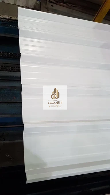 صفيحة معدنية بيضاء مضلّعة ممتدة على ماكينة تشكيل زرقاء داخل مصنع ألواح