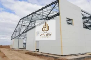 هيكل معدني بجمالونات ظاهرة أثناء كسوة جدرانه بألواح معزولة بيضاء مع فتحات نوافذ محدّدة الإطار