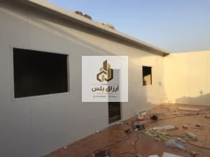 جدران خارجية من ألواح معزولة بفتحة نافذة كبيرة وفتحة باب داخل فناء مبلّط مع بقايا قص على الأرض