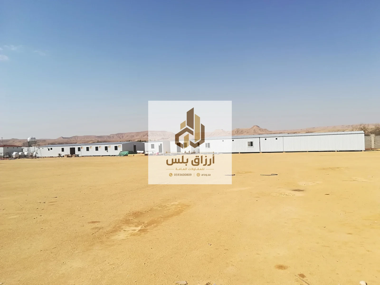 صف طويل من وحدات جاهزة من ألواح معزولة على أرض صحراوية واسعة وجبال في الخلفية