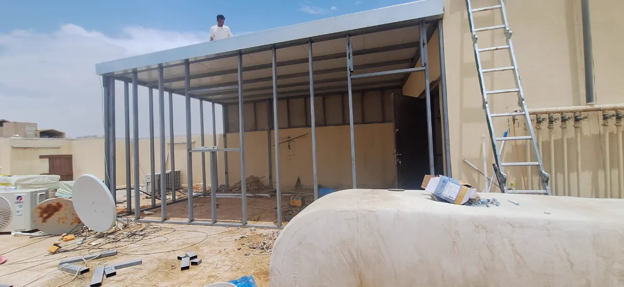 هيكل معدني قيد التركيب على سطح مبنى مع سلّم وشخص أعلى الهيكل