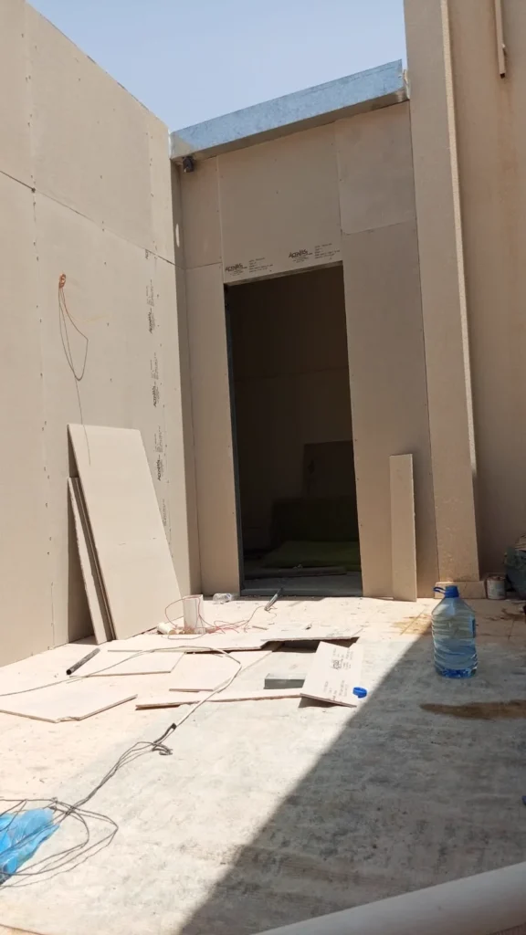 فناء داخلي محاط بجدران ساندوتش بانل مع فتحة باب وألواح احتياطية مسنودة على الجدار