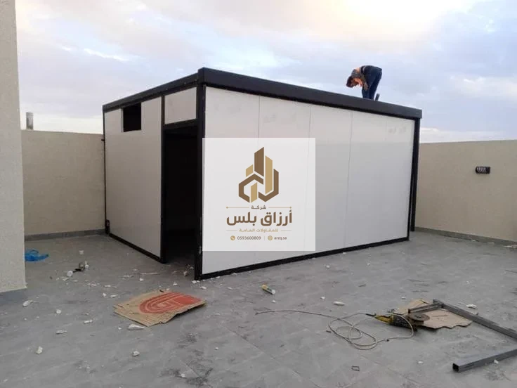 غرفة ساندوتش بانل على سطح مبنى أثناء التركيب، يظهر إطارها الأسود وفتحتا الباب والنافذة قبل إكمال التشطيب