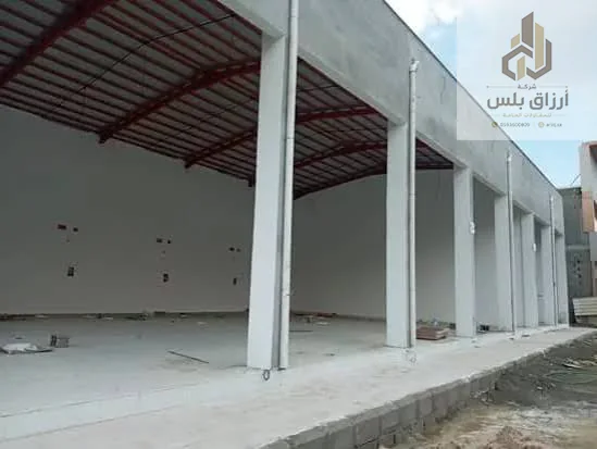 مستودع مفتوح من الداخل بأعمدة بيضاء وجمالونات حديدية حمراء وأرضية خرسانية